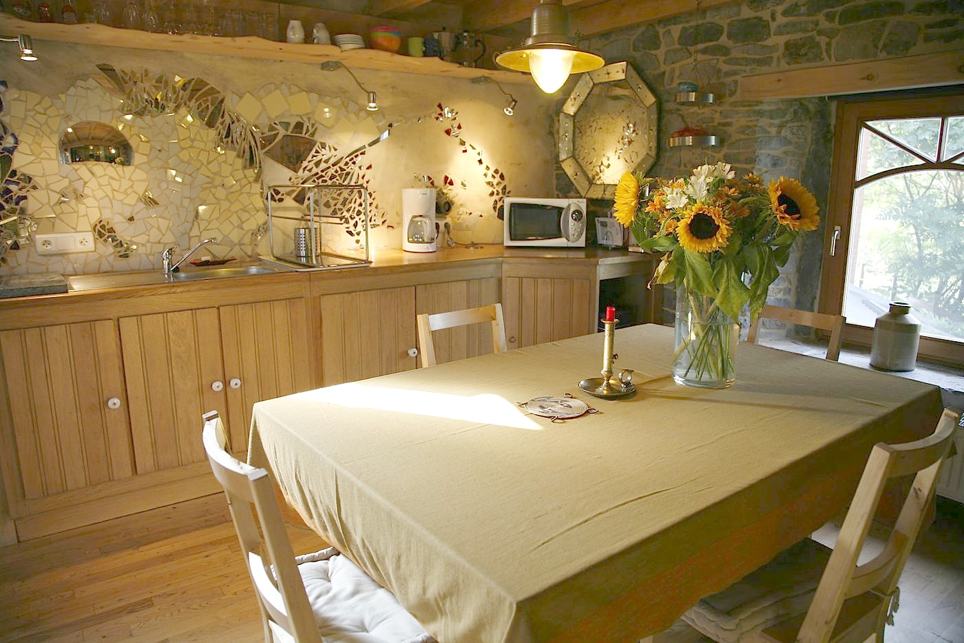 Cuisine du gîte habillée d'une mosaïque de tournesols, pierre et bois en lumière chaude